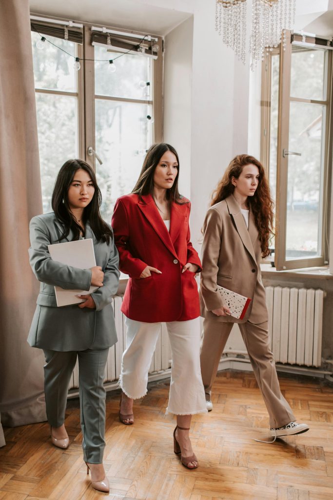 Three diverse women in business attire confidently walking in an office hallway.